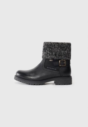 Bottines noires avec un revers en tricot gris texturé, dotées d'une boucle sur le côté et d'une semelle en caoutchouc avec des crampons pour l'adhérence. Tige en cuir lisse.