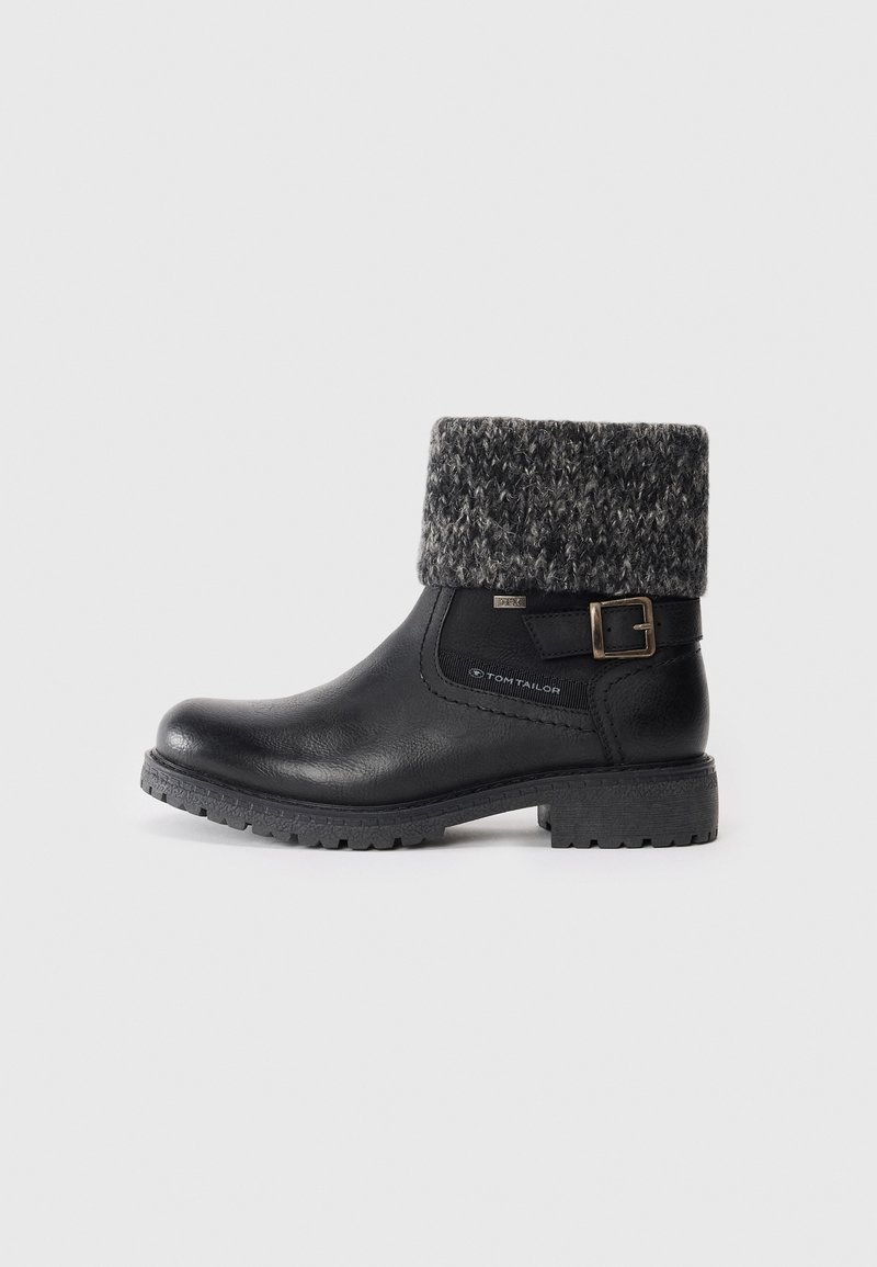 Bota de tornozelo preta com um punho em malha cinza texturizada, apresentando uma fivela lateral e uma sola de borracha com aderência. Parte superior em couro liso.