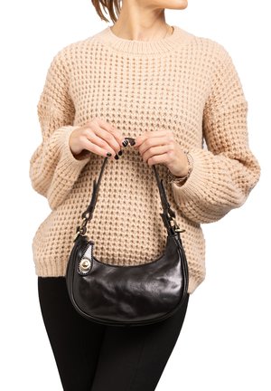 Borsa in pelle nera dalla forma curvata e con una tracolla corta. Presenta dettagli in metallo dorato e cuciture. Il maglione è in maglia spessa, beige.