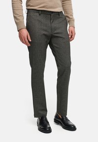 Pantalones grises texturizados con corte recto, que presentan trabillas y bolsillos laterales, combinados con mocasines de cuero negros.
