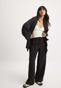 Svart kimono-jacka över en vit, åtsittande tube-top. Löst sittande svarta byxor med texturerad yta och svarta sandaler med ljusa remmar.
