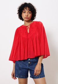 Rote, locker sitzende Bluse mit gerafftem Ausschnitt, Schlüssel-Loch-Detail und fließenden Ärmeln, kombiniert mit Denim-Shorts.