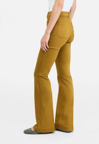 Ausgestellte Senfgelb-Hosen aus einer Baumwollmischung, mit Gesäßtaschen und einer taillierten Taille. Tragen mit schwarz-weißen gemusterten Ballerinas.