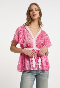 Top rosa con motivo a fantasia, maniche a farfalla corte, scollatura a V e bordo in pizzo bianco, caratterizzato da un laccetto con frange decorative bianche.