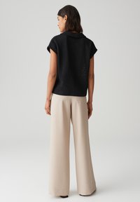 Top corto nero in tessuto strutturato con colletto, abbinato a pantaloni larghi beige. Il top presenta un sottile motivo a maglia aperta sul retro.