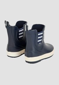 Bottes en caoutchouc marine à chevilles avec semelle blanche, doublure en tissu rayé et languettes de tirage. Elles présentent une texture lisse et un design arrondi.