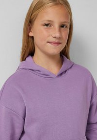 Fialová mikina s měkkou strukturou a přední kapsou typu "klokan". Má pohodlný střih, kapuci a žebrované okraje.