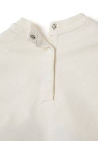 Close-up van een beige stoffen shirtkraag met twee snaps losgemaakt, die de geribbelde textuur aan de rand van de kraag toont.