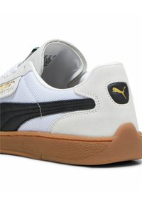Sneaker bianca e nera con una tomaia testurizzata, suola in gomma color caramello, dettagli in oro e collarino imbottito per il comfort.