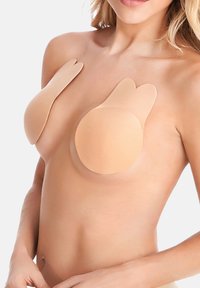 Nude samolepicí prsní vycpávky s zaobleným tvarem a křidélky ve tvaru srdce pro dodatečnou podporu, navržené pro bezproblémové nošení pod oblečením.