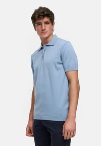Polo de manga corta azul claro hecho de un tejido de punto suave, con cuello y tapeta de tres botones, y con bordes acanalados.