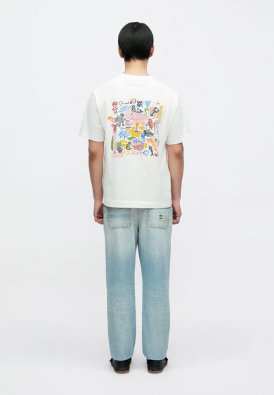 Άσπρο T-shirt με κοντά μανίκια και πολύχρωμο γραφικό σχέδιο στην πλάτη. Φορεμένο με ανοιχτόχρωμα γαλάζια τζιν με επιδιόρθωση και άνετη εφαρμογή.