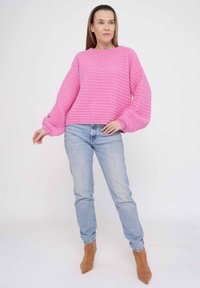 Rosa gestrickter Pullover mit strukturierten Streifen, rundem Halsausschnitt und voluminösen Ärmeln, kombiniert mit hellblauen Jeans und beigen Knöchelboots.