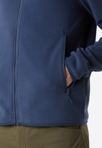 Giacca in pile navy con chiusura a zip, dotata di tasche laterali e una texture liscia. Le maniche sono a polsino e l'orlo si ferma all'altezza della vita.