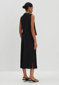 Schwarzes ärmelloses Oberteil mit hohem Kragen, kombiniert mit einem passenden knöchellangen Rock mit seitlichen Schlitzen und schwarzen Riemchensandalen.