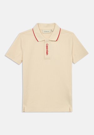 Béžové polo tričko s krátkými rukávy, červeným lemováním na límci a vertikálním logem Calvin Klein na légě.