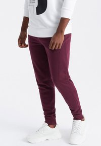 Burgunderrote Jogginghose mit elastischen Bündchen und seitlichen Nähten, kombiniert mit weißen Turnschuhen. Der Bund ist elastisch für mehr Komfort.
