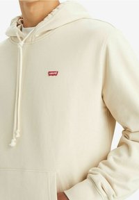 Felpa beige con tasca frontale, cappuccio regolabile con coulisse e logo rosso Levi's sul petto. Realizzata in un morbido tessuto testurizzato.
