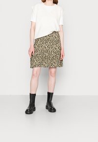 Maglione senza maniche a V, crema, indossato sopra una gonna a fantasia al ginocchio in tonalità terrose con accenti in bianco e nero, abbinato a stivali neri alla caviglia.