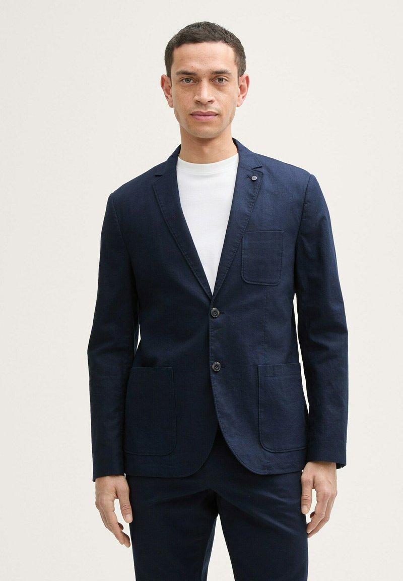 Sacou din in navy cu două buzunare frontale și rever cu formă trapezoidală, având închidere cu un singur nasture și un design minimalist.