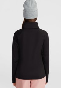 Svart långärmad topp med hög krage, tillverkad av slätt tyg. Har raglanärmar och en åtsittande design, vilket kombineras med en grå mössa.
