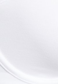 Sujetador de tela blanca con textura suave y acolchado blando. Presenta una forma curva y costuras resistentes a lo largo de los bordes.