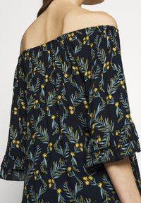 Blusa floral de hombros al aire en negro, con patrones botánicos en amarillo y verde, mangas con volantes y una tela suave y ligera.