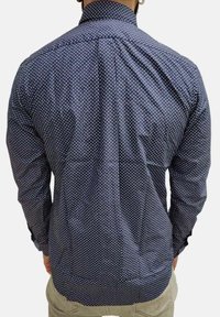 Camicia abbottonata blu navy con piccoli pois bianchi, maniche lunghe e colletto standard. Tessuto liscio con un aspetto texture.