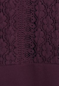 Texturovaná tmavě fialová tkanina s propracovanými krajkovými vzory a pevnými pletenými sekcemi. Krajka vykazuje květinové motivy a otevřené vazby.