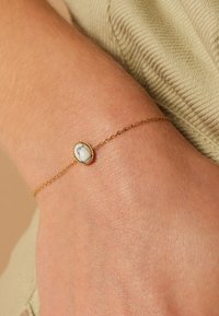 Gold chain bracelet with an oval white stone centerpiece, featuring a textured edge and a delicate link design.