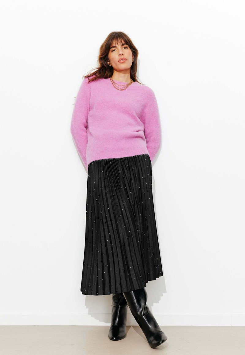 Pull rose duveteux à col rond associé à une jupe noire plissée ornée de points argentés. Des bottines noires viennent compléter ce look.