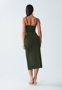 Olive green, knee-length dress with spaghetti straps, fitted silhouette, and smooth texture, paired with beige high-heeled shoes.