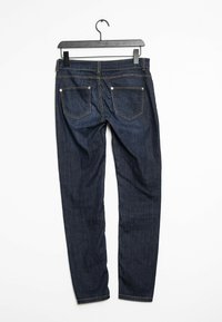 Jeans de mezclilla azul oscuro con un corte ajustado, bolsillos traseros y detalles de costura clara. Cuélganse en una percha negra contra un fondo blanco.