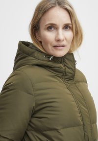 Oliivroheline puffjakker, millel on kapuuts, ees lukuga, õmblustega ja sileda tekstuuriga. Kapuutsi peal on reguleeritavad nöörid.