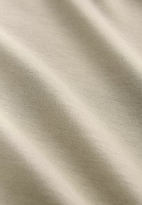 Svijetlo bež pamuk s glatkom teksturom, prikazuje suptilne, fine tkanja i blage nabore, bez vidljivih uzoraka ili dodataka.