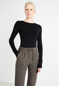 Top nero a maniche lunghe con scollatura rotonda abbinato a pantaloni marroni a vita alta con motivo, dotati di una cintura e pieghe frontali.