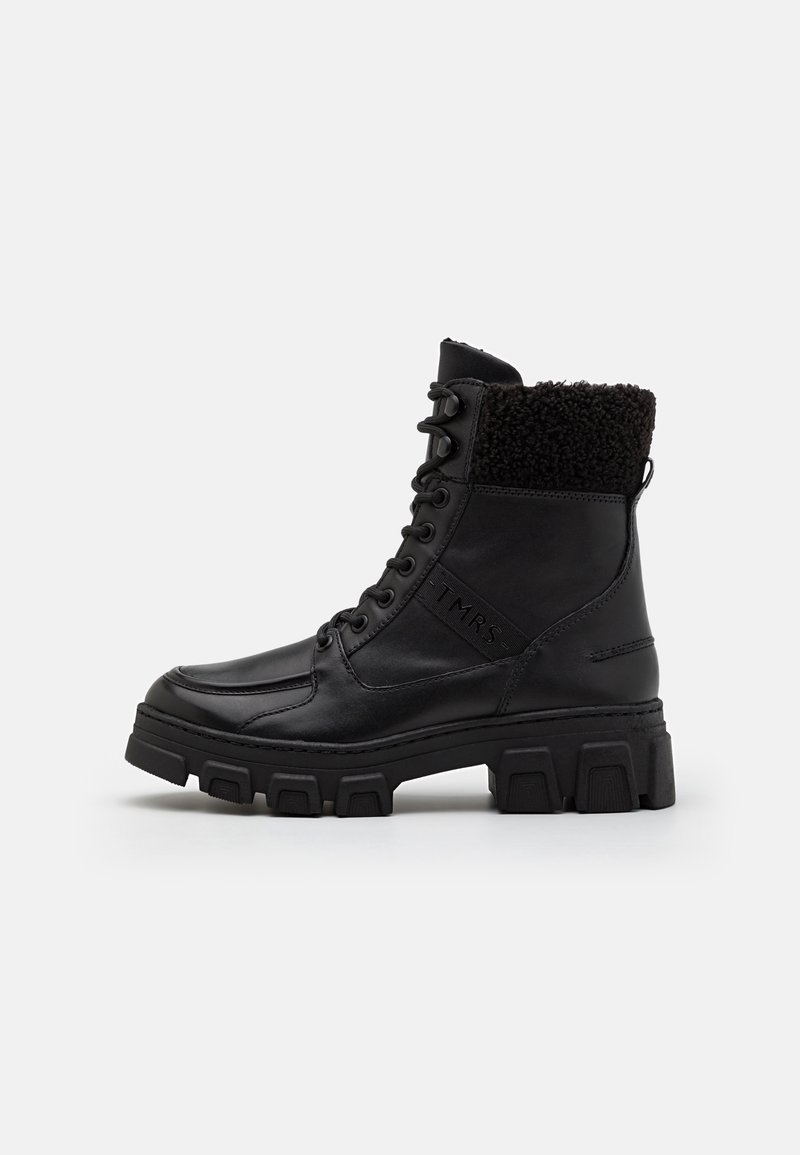 Botte noire en cuir à lacets avec semelle épaisse à crampons et bord en polaire texturée, marquage latéral et languette de tirage au talon.