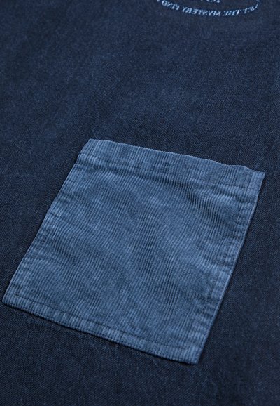 Gros plan d'une poche en velours côtelé bleu cousue sur un fond de tissu bleu foncé.