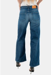 Jeans de mezclilla de pierna ancha en azul, con un lavado claro, cinturilla de altura media, dos bolsillos traseros y una etiqueta de cuero en la cintura.