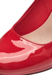Raudoni lakiniai bateliai su apvaliu nosimi, lygia blizgia apdaila ir minkšta, apmušalu iš audinio vidumi. Minimalus siuvinėjimo detalė palei kraštą.