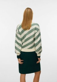 Sweter dziewiarski z oversize'owymi rękawami, w zielono-kremowe ukośne paski. Połączony z ciemnozieloną spódnicą w prążki.
