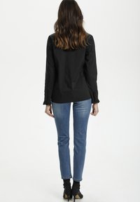 Melnas garām piedurknēm bl�ūze ar teksturētām detaļām pie aprocēm, apvienota ar pieguļošām zilo džinsu biksēm un potīšu zābakiem. Vienkāršs, pielāgots dizains.