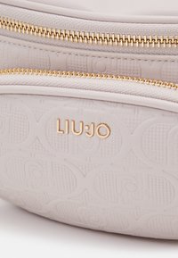 Borsa a tracolla beige chiaro con superficie testurizzata, dotata di cerniere in metallo dorato e dettagli con logo impresso. Design liscio e strutturato.