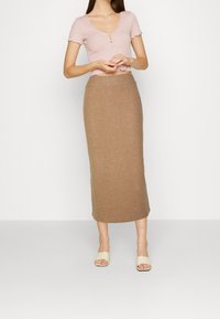 Ljusrosa kortärmad topp med scallop-kant och tre knappar, ihop med en brun stickad kjol som når anklarna. Bärs med beige slidesandaler.