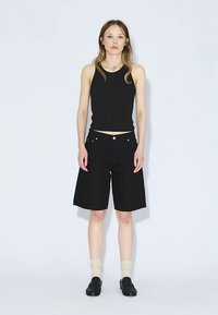 Camiseta sin mangas negra combinada con pantalones cortos negros hasta la rodilla, con un corte recto, diseño minimalista y sutiles detalles naranjas en los bolsillos.
