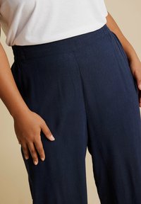 Granatowe spodnie szerokie z elastycznym pasem, wykonane z miękkiej tkaniny, o gładkiej strukturze i luźnym kroju.