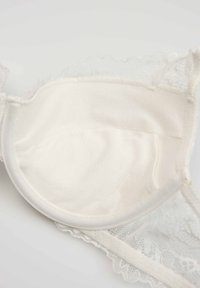 Miękka wkładka do biustonosza z białej koronki z wyściełanym wnętrzem z tkaniny oraz delikatną koronkową lamówką na białym tle.