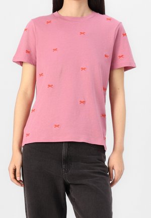 Camiseta de manga corta rosa con escote redondo y lazos bordados en naranja repartidos. Confeccionada en suave tela de algodón, presenta un corte holgado.