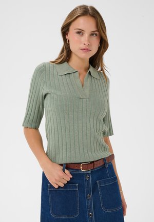 Tricou polo cu mâneci scurte, verde, cu model în dungi și guler, combinat cu o fustă din denim ce are buzunare mari în față și o curea maro.