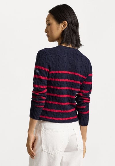 Pull en maille torsadée bleu marine avec des rayures horizontales rouges, doté d'un col rond, de poignets côtelés et d'un petit logo brodé sur la manche.